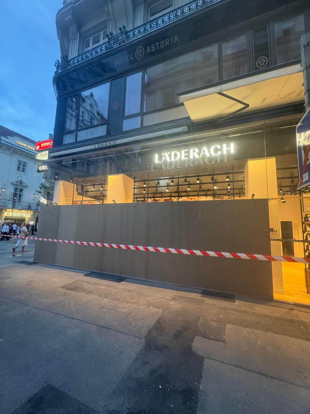 Zerbrochene Glasfassade von Läderach Wien 1010 nach Vandalismus, Polizeiabsperrung sichtbar